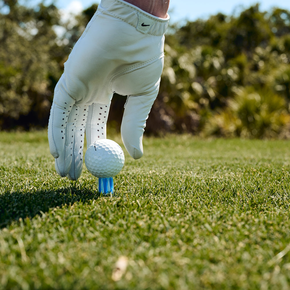 hand placing golf ball onto blue brush tee. reduce friction.