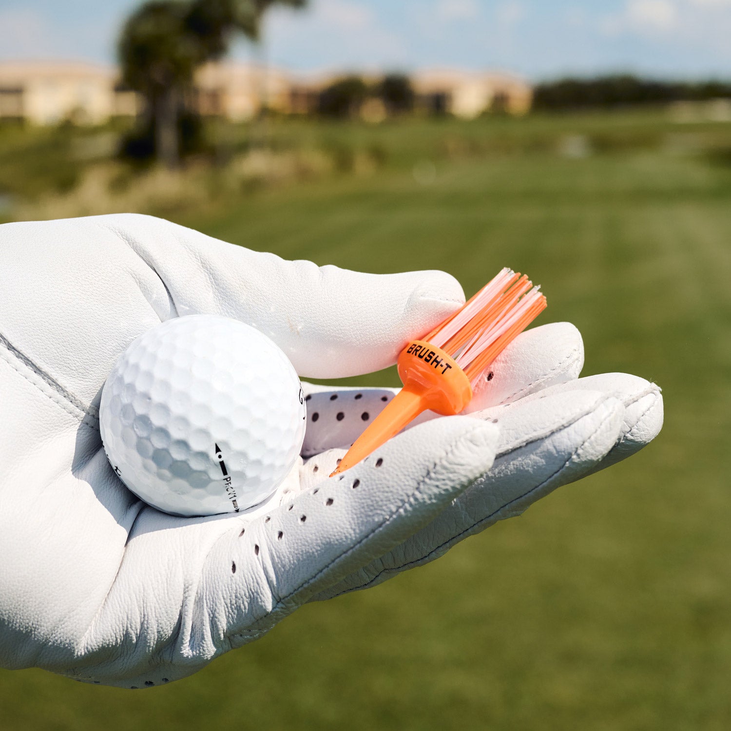 golf glove hand holding orange brush tee.